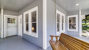 A covered porch with a wooden bench, white shutters, and a door.