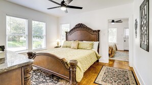 A bedroom with a large bed, a ceiling fan, and a view of the outdoors through the windows.
