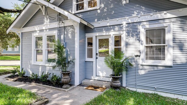 A two-story house with a front porch, a garage, and a small front yard with potted plants.
