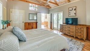 Un dormitorio con una cama grande, vigas de madera en el techo, un ventilador de techo, un televisor y un aparador.