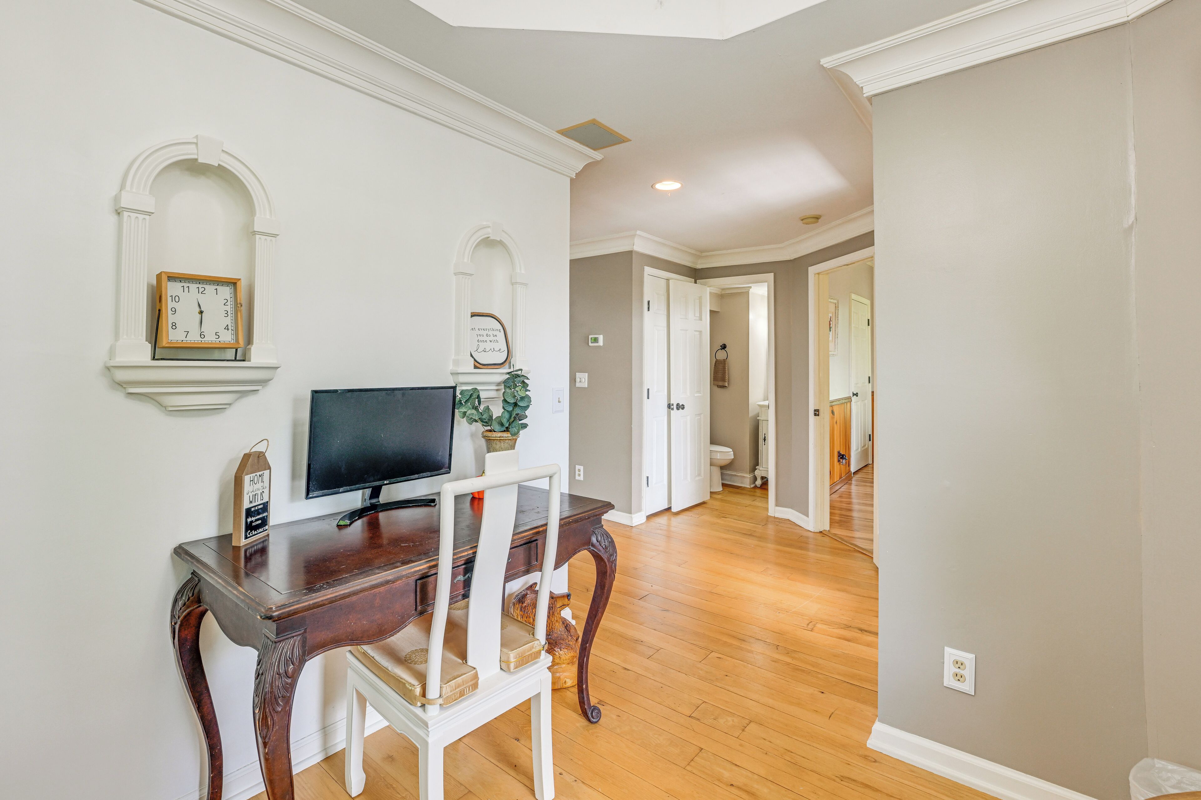 A room with a wooden desk, a chair, a television, and a clock on the wall.