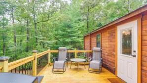 A wooden deck with two chairs and a table, surrounded by a wooden railing, overlooking a forested area.