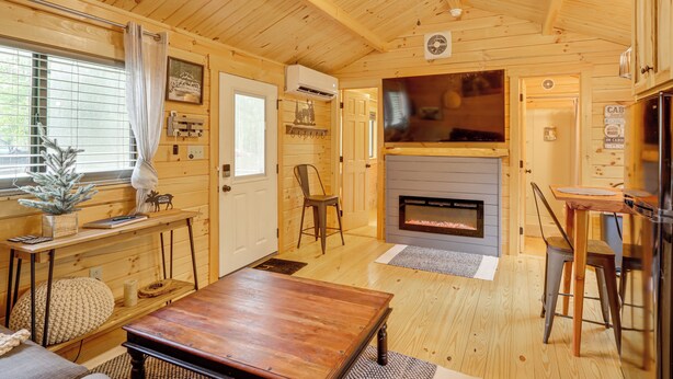 A cozy cabin interior with a wooden ceiling, a fireplace, a dining table, and a TV mounted above it.