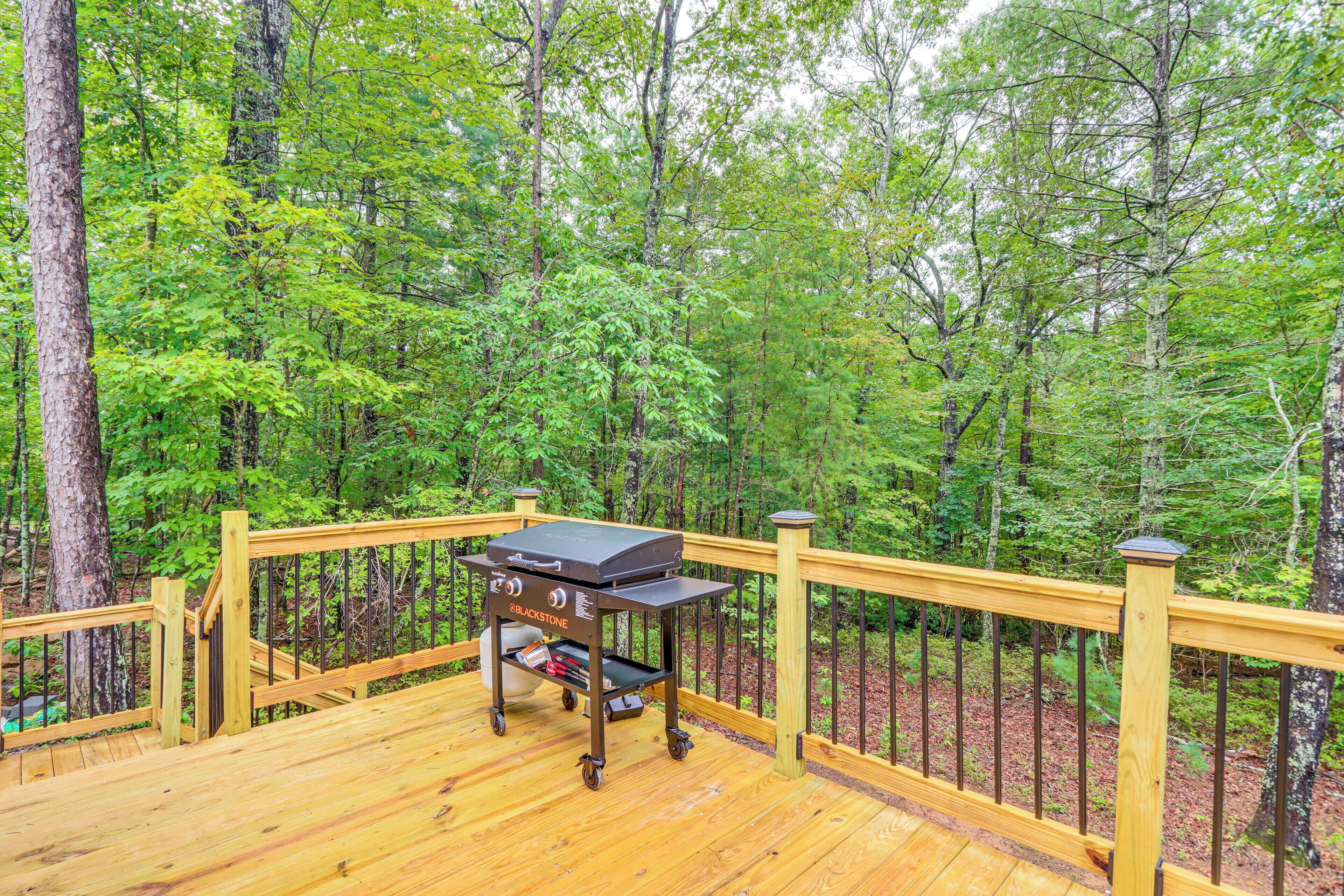 A deck with a grill cart in a forested area.