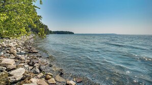 A rocky shoreline with clear water and a distant tree-covered island. - Grill Out, Play Pool: Huge Home on Lake Champlain! (Chazy)