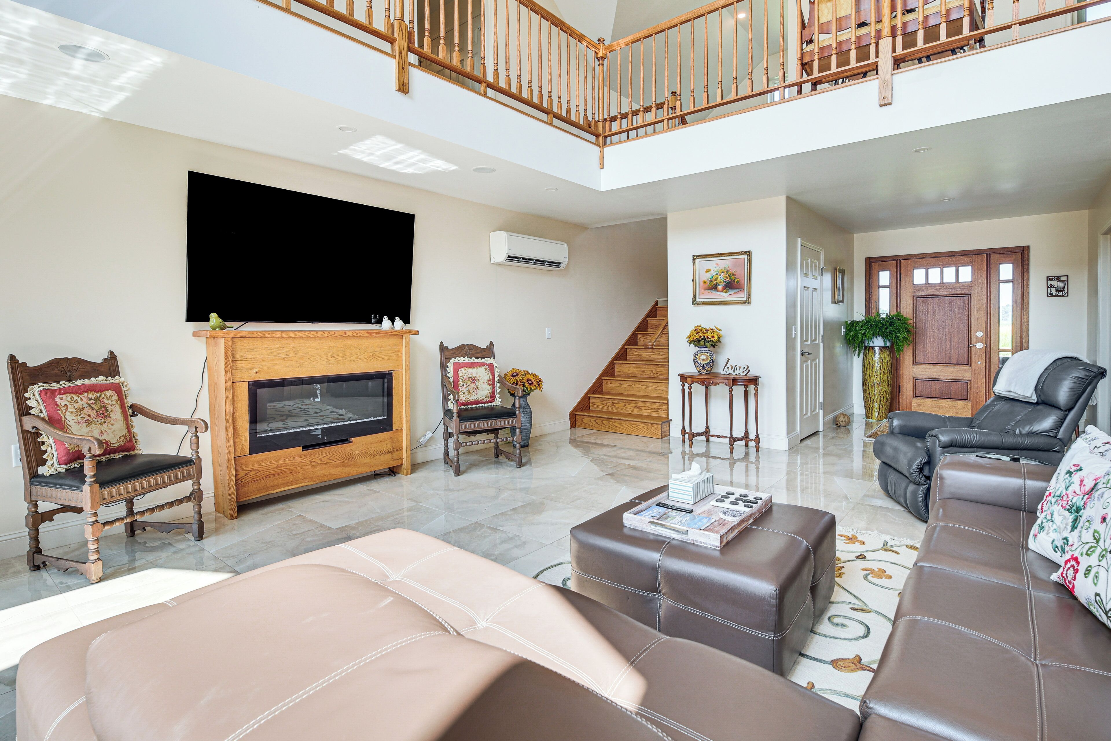 A spacious living room with a fireplace, leather sofas, a TV, and a staircase leading to an upper level.