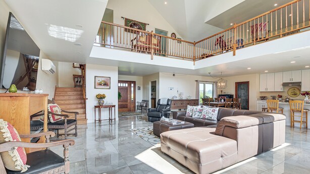 A spacious living area with a high ceiling, a wooden staircase, and a balcony. - Grill Out, Play Pool: Huge Home on Lake Champlain! (Chazy)