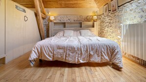 Quarto com teto de madeira, parede de pedra, cama com cabeceira e duas luminárias fixadas na parede.