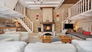A spacious living room with a fireplace, white sofas, a wooden coffee table, and a staircase with white railings.