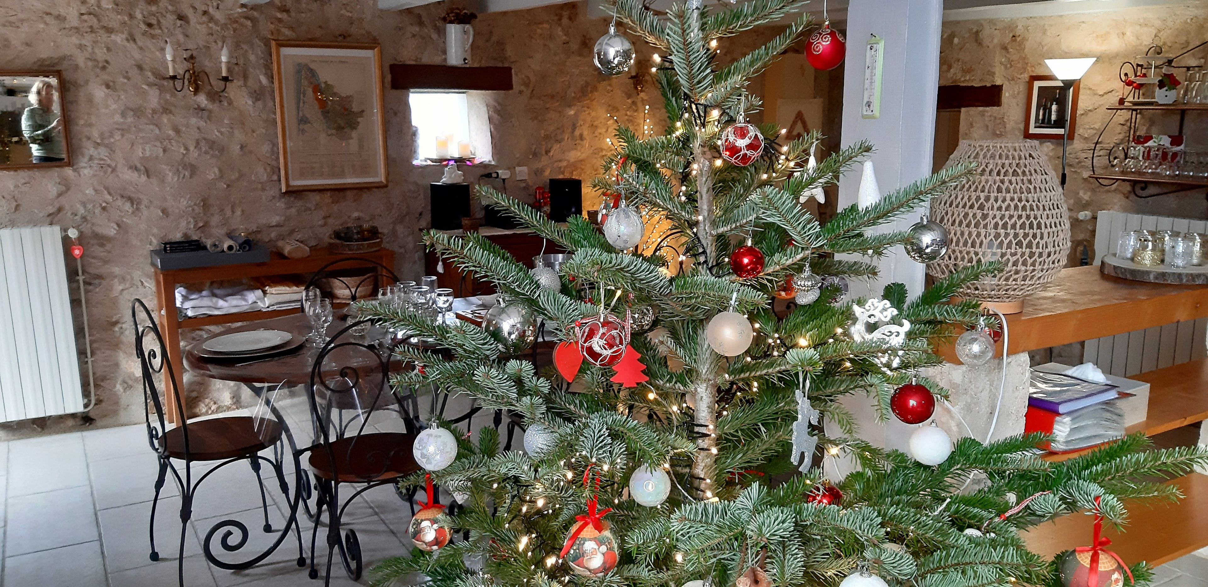 Une pièce avec un sapin de Noël décoré, une table à manger entourée de chaises et un mur en pierre rustique.