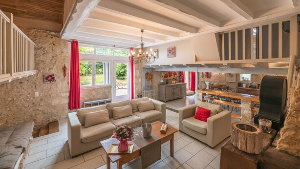 A spacious living room with a stone wall, a wooden ceiling, and a fireplace.