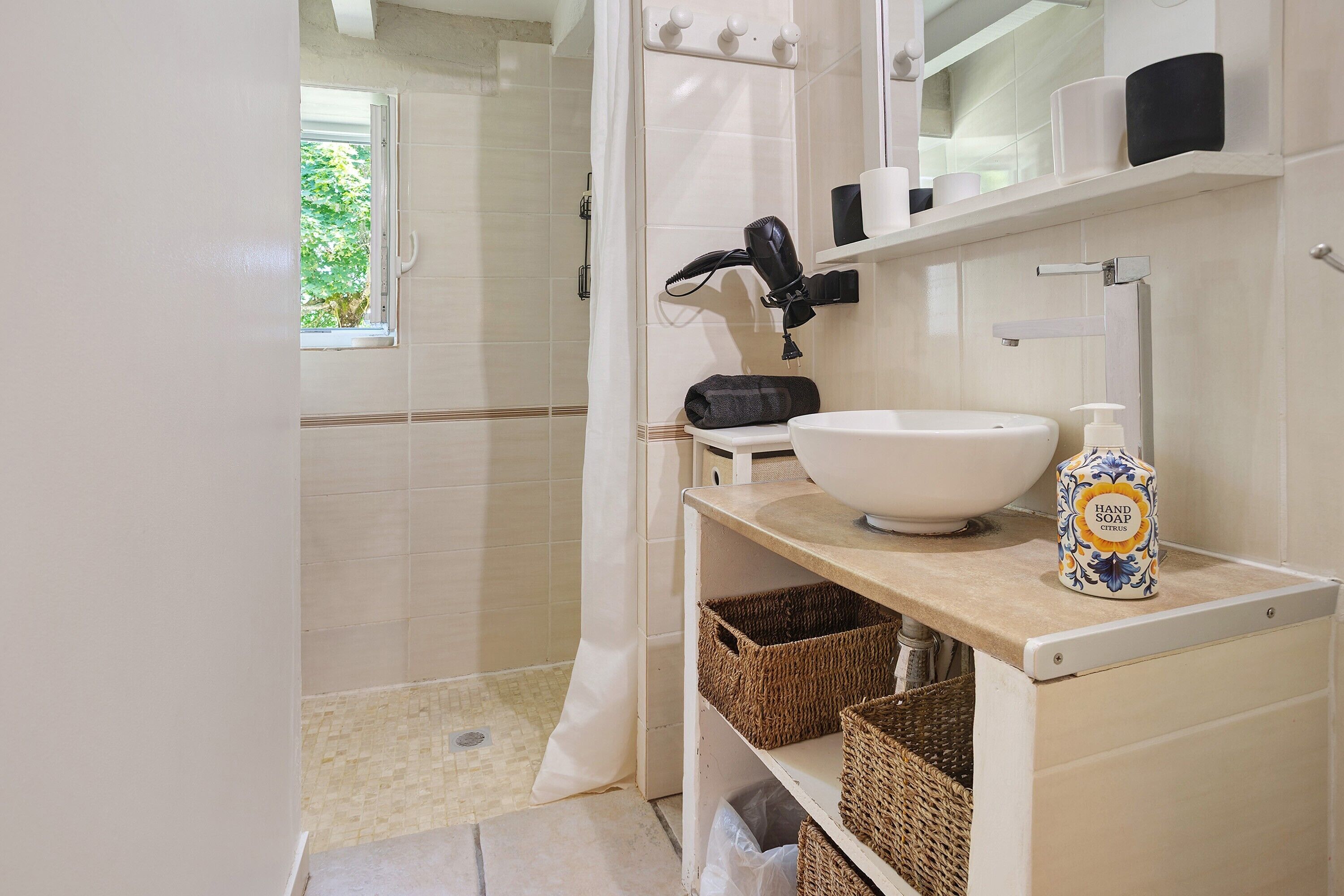 A bathroom with a white sink, a hairdryer, a bottle of hand soap, and wicker baskets.