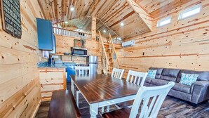 L’intérieur d’un chalet en bois comprend une table à manger, des chaises blanches, un canapé et un coin cuisine.