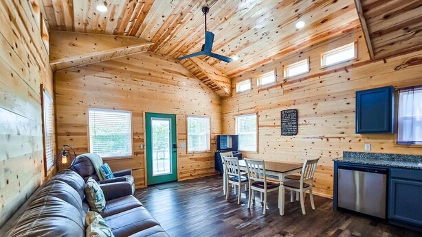 L’intérieur d’un chalet en bois comprend un canapé, une table à manger, des chaises, un téléviseur et un coin cuisine.