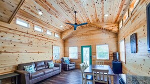 L’intérieur d’une cabane en rondins comprend un coin repas, un ensemble de canapés et un ventilateur de plafond.