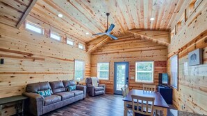 A log cabin interior with a sofa, recliner, dining table, and ceiling fan.