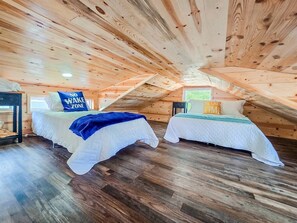 Un dormitorio en el ático con dos camas, vigas de madera y una ventana.