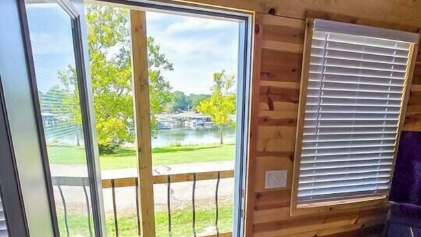 A wooden cabin interior with a sliding glass door leading to a deck, a window with blinds, and a doormat.