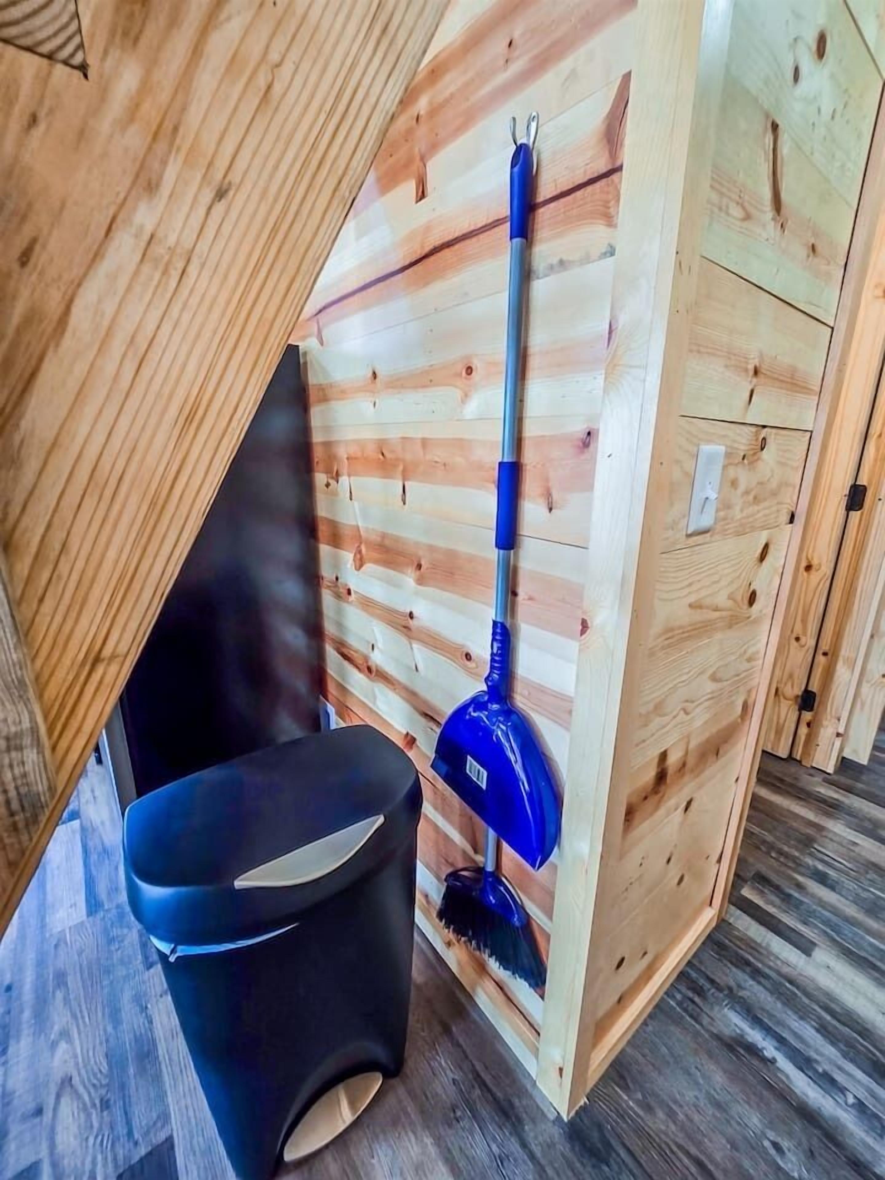 Una habitación con techo inclinado, una escoba azul y una silla negra.