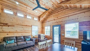 A log cabin interior with a sofa, chairs, a dining table, and a ceiling fan.