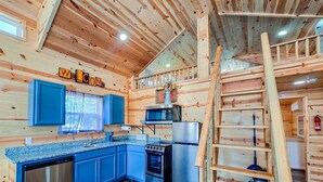 L’intérieur d’un chalet en bois, avec une cuisine, une porte bleue et une échelle en bois.