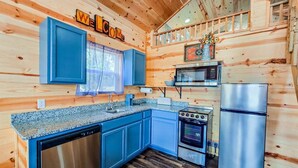 L’intérieur d’un chalet en bois comprend une cuisine avec des meubles bleus, un réfrigérateur en acier inoxydable, une cuisinière et un four à micro-ondes.
