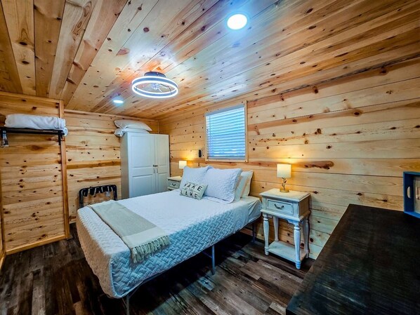 A wooden cabin bedroom with a bed, bedside tables, a window, and a ceiling light fixture.