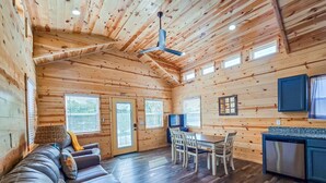 A cabin interior with a sofa, dining table, chairs, a TV, and a kitchen area.
