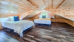 A cozy attic bedroom with two beds, wooden walls, and a small window.