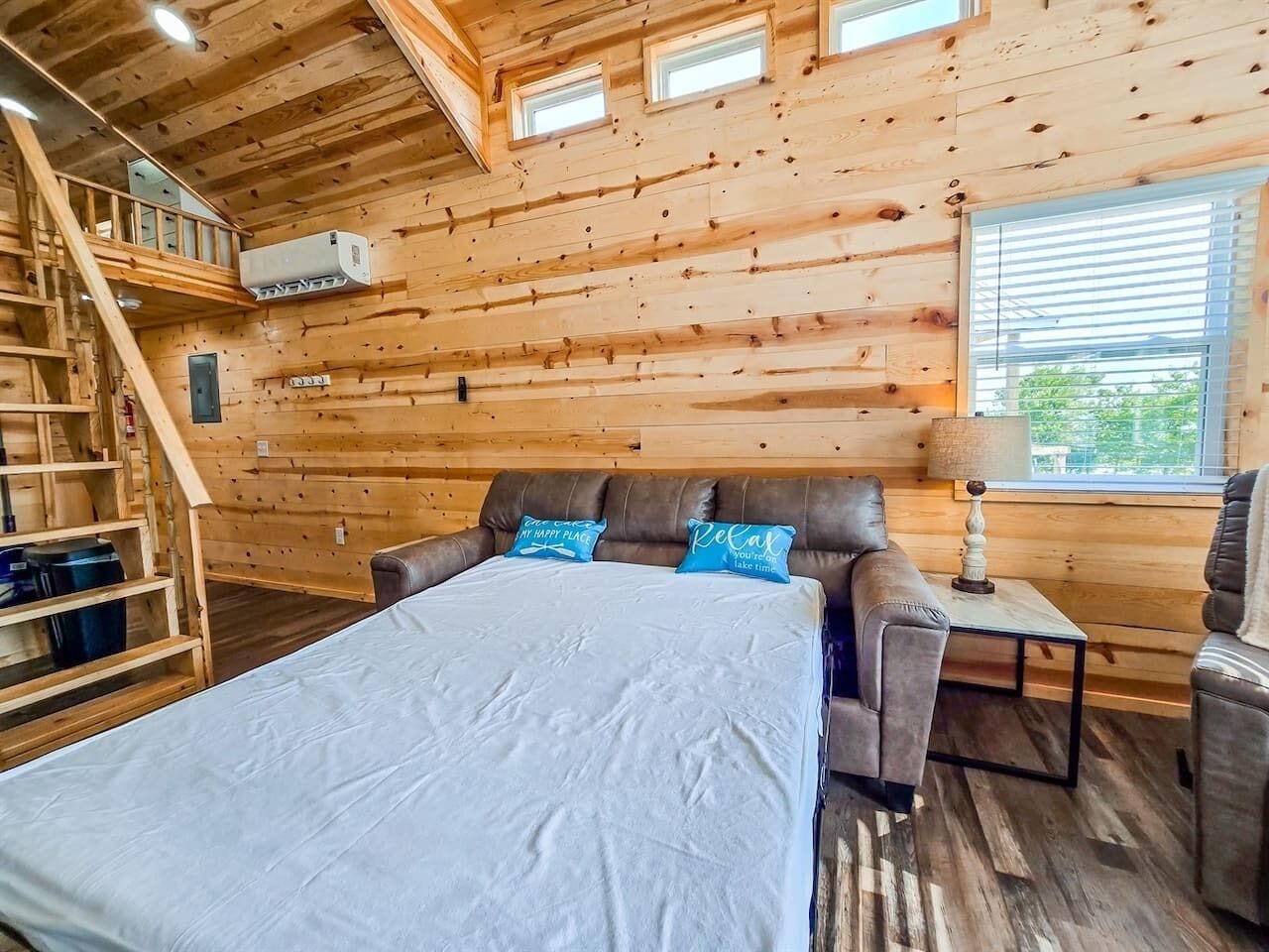 Interno di una baita in legno con un letto, una poltrona, un tavolo e una scala.