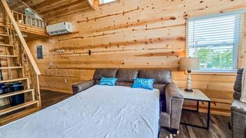 Interno di una baita in legno con un letto, una poltrona, un tavolo e una scala.
