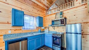 Una cocina con paredes de madera, armarios azules, un refrigerador de acero inoxidable y una estufa.