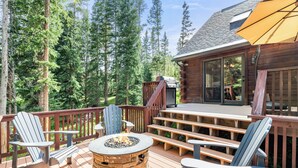 Une terrasse en bois avec des fauteuils Adirondack, un foyer et un grand parasol.