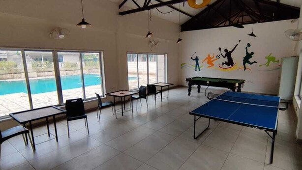 Un grand espace intérieur comprenant une table de ping-pong, plusieurs chaises et une vue sur la piscine.