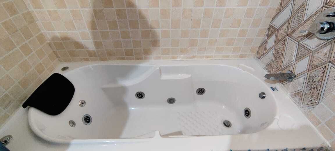 Una bañera blanca con un asiento negro, varios orificios de desagüe y una base texturizada.