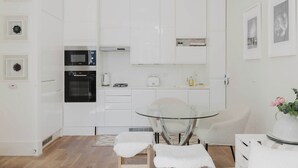 A modern kitchen with white cabinets, a glass table, and a white chair.