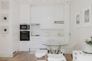 A modern kitchen with white cabinetry, a glass dining table, and a white sofa. - Chic 1BD Flat in Historic Building, East London (Greater London)