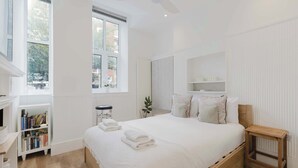 A bedroom with a large bed, a bedside table, a bookshelf, and a window.