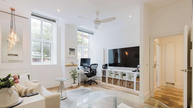 A modern living room with a flat-screen TV, a ceiling fan, and a large window.