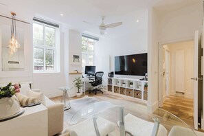 A modern living room with a flat-screen TV, a ceiling fan, and a large window. - Chic 1BD Flat in Historic Building, East London (Greater London)