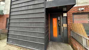 A building entrance with a metal siding exterior, a brick wall, and a door with a sign reading 'STILMAN PLACE'.