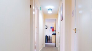 Un couloir étroit, doté d’un revêtement de sol en moquette et de murs blancs, qui mène à une pièce contenant un bureau et une chaise.