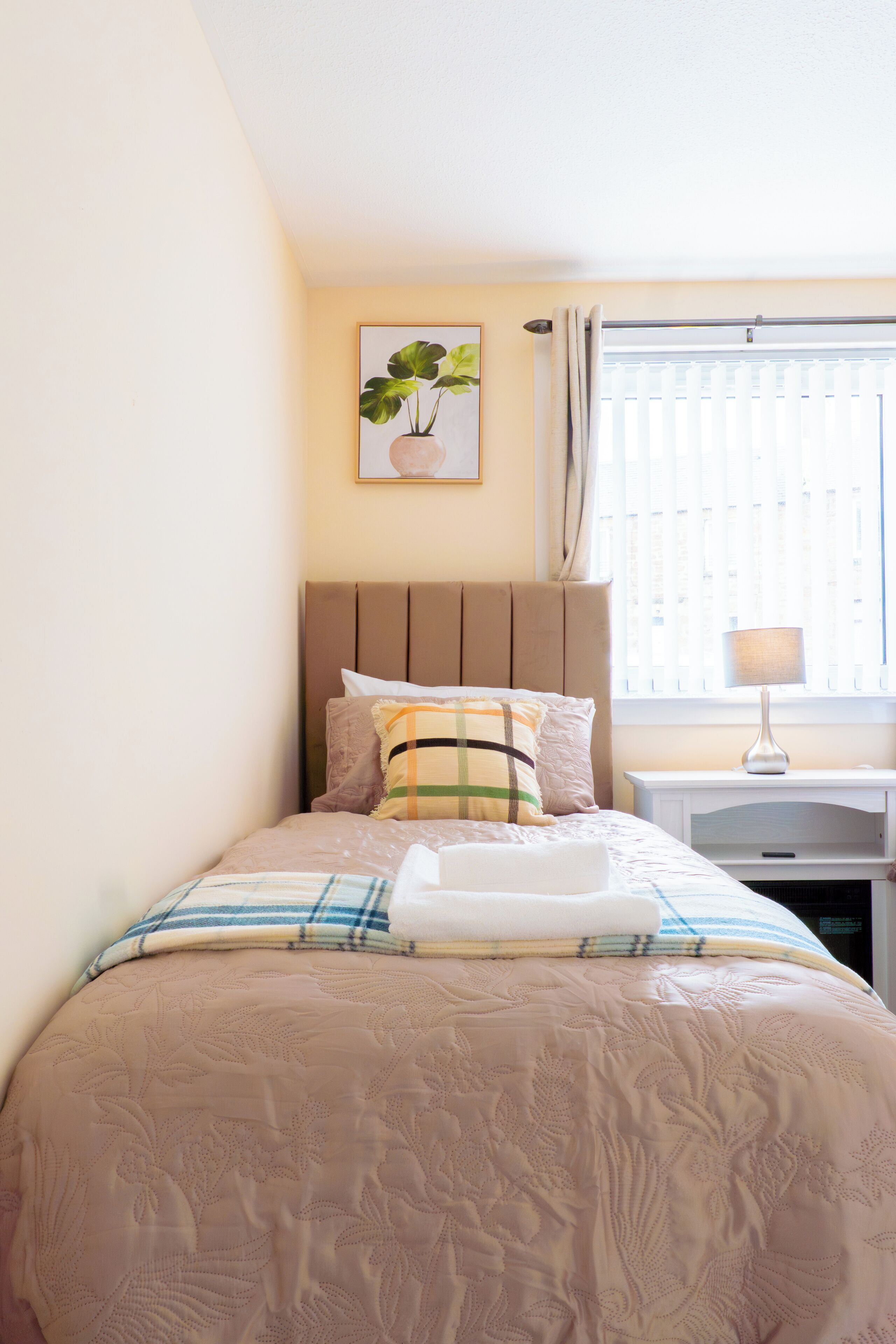 A neatly made bed with a floral-patterned bedspread, a headboard, and a bedside table with a lamp.