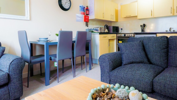 Un salon moderne avec un canapé, une table à manger et des chaises, et un coin cuisine à l’arrière-plan.