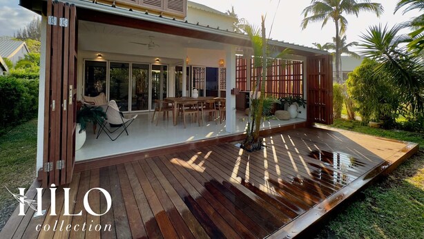 Una casa moderna con terraza de madera, ventanas grandes y una zona de estar exterior cubierta.