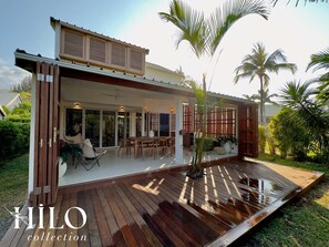 A modern house with a wooden deck, large windows, and a covered outdoor seating area.