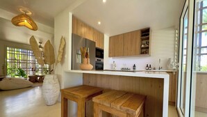 Una cocina moderna con armarios de madera, una encimera blanca y un horno empotrado. Hay dos taburetes de madera y un jarrón grande con plantas secas.