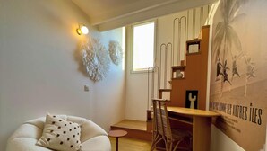 Una habitación moderna con un sofá blanco, una mesita redonda pequeña, una silla de madera, una lámpara de pared y un cartel.