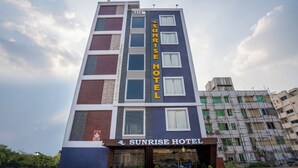 Un hôtel à plusieurs étages, reconnaissable à son grand panneau indiquant « Sunrise Hotel ».