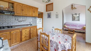 Una cocina con armarios de madera, salpicadero de azulejos, una mesa de comedor con sillas y una sala de estar con sofá y televisor montado en la pared.